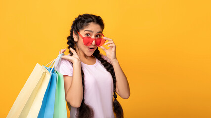 Indian ladywoman in glasses holding colorful shopping bags at studio