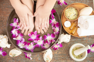Fototapeta na wymiar closeup view of woman soaking her hand and feet in dish with water and flowers on wooden floor. Spa treatment and product for female feet and hand spa. orchid flowers in ceramic bowl.