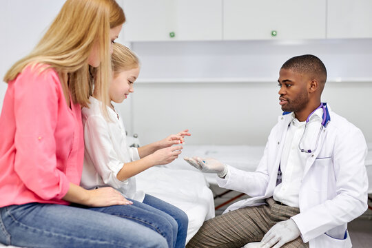 black male doctor have a nice talk with kid girl, showing colourful modern capsules to her, he disposes, work with children in hospital