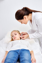 piercing ears to caucasian child girl in medical salon by a doctor in white robe using a special device. beauty and medicine concept