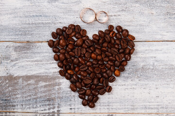 Heart coffee and wedding rings. Heart made of coffee beans on white wood.