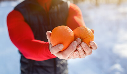 Closeup of fit mature man holding oranges as healthy snack after morning workout at snowy winter forest, panorama