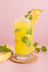 Pineapple cocktail or fresh pineapple juice, mint leaves in glass with ice and  pineapples on a pink background. selective focus.