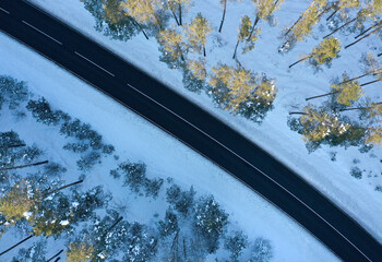 Aerial view of the winter road in the snowy forest with trees covered with snow. 