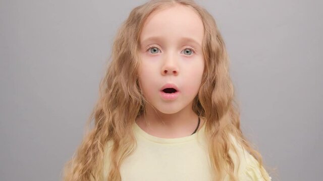 Little girl is surprised looking into the camera. Picture taken in the studio on a gray background. Super slow motion.