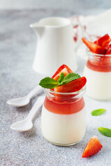 Festive dessert with berry jelly, vanilla panna cota and fresh strawberry on gray concrete table background. Selective focus.