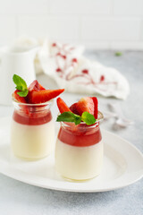 Festive dessert with berry jelly, vanilla panna cota and fresh strawberry on gray concrete table background. Selective focus.