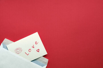 Handmade postcard with mark of lips and lettering love from envelope on red background