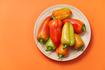 The colored pepper lies on a slide on a wooden plate on a orange background with text area. The view from the top.