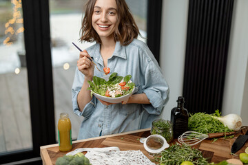 Portrait of young woman smiling and eating healthy green salad with tomato freshly cooked at home....