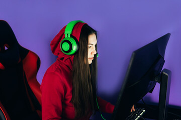 A young girl playing a computer game on professional armchair against monitor in green headphones, live stream, esports
