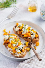 Baked pumpkin sandwich with dorblu cheese with blue mold, honey and thyme on a concrete old light background. Top view.