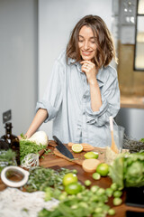 Pretty woman with green ingredients thinking about cooking healthy food on the kitchen. Healthy and...
