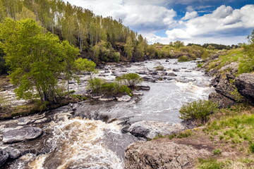 Summer landscape with fast-flowing river, stone banks, trees and blue sky with white clouds