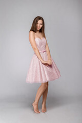 Fototapeta premium Young beautiful girl in a pink dress stands on a gray background