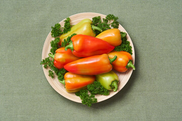 The colored bell pepper and parsley lies on a slide on a wooden plate on a green napkin. The view from the top.