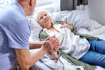 mature female patient at hospital with worried husband holding hands while checking blood pressure with tonometer. man helps, support