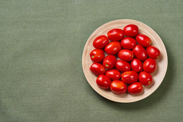 Whole small tomatoes in a wooden plate is on a green napkin with text area. The view from the top.