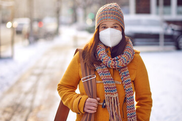 Middle-aged brunette woman in winter clothes wearing face mask outdoors due to Corona virus outdoors while on her way to work - obrazy, fototapety, plakaty