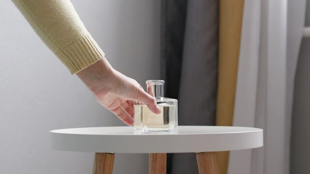 Home perfume aroma diffuser on white coffee table in room. Woman puts wooden sticks in aroma diffuser