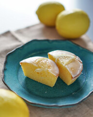 Moist and Sweet Lemon Butter Cake flavored with Lemon Juice Glaze Icing and Zest, garnished with a lemon slice. Soft and Sour Cream Lemon Dessert, putting on a blue plate, decorate with fresh lemons.