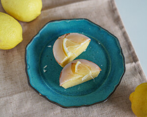 Moist and Sweet Lemon Butter Cake flavored with Lemon Juice Glaze Icing and Zest, garnished with a lemon slice. Soft and Sour Cream Lemon Dessert, putting on a blue plate, decorate with fresh lemons.