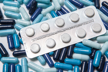 Pills in blister on pile of colorful medicament capsules