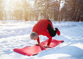 Fit senior man having outdoor yoga practice in winter at snowy forest