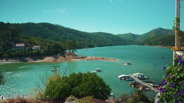 Lake pier with sport boats at marina with swimming people, padle practicing among mountain pine trees at sunshine in wide shot 4K