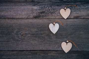 Valentine's Day background. Brown natural boards in grunge style with three wooden decorative hearts. Top view. Surface of table to shoot flatlay. Concept love, romantic relation. Copy space for text.