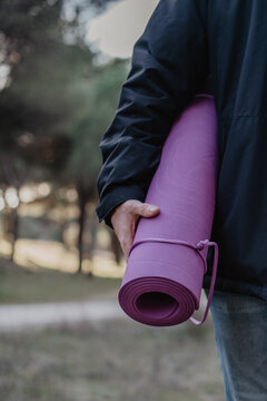 Imagen vertical de un hombre sujetando una esterilla para hacer yoga o pilates de color morado. Concepto de deporte al aire libre