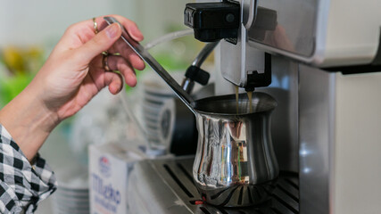 the waitress is preparing latte and Coffee in a white cup with milk foam in a coffee maker