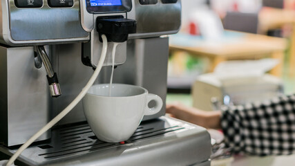 the waitress is preparing latte and Coffee in a white cup with milk foam in a coffee maker
