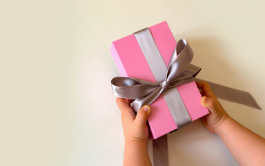 child hands holding pink gift box with silver bow