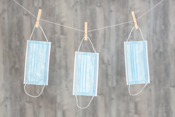 Drei aufgeh&auml;ngte OP-Masken an der Leine vor einem Holzhintergrund