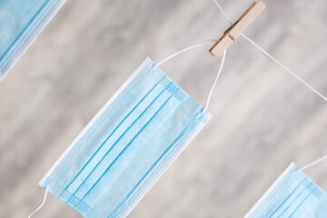 eine aufgeh&auml;ngte OP-Maske an der Leine mit einer W&auml;scheklammer vor einer Holzwand 