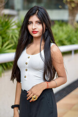 Obraz premium Portrait of very beautiful straight haired young attractive Indian woman wearing white and black outfit standing in a blurred background. Lifestyle and Fashion.