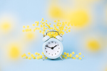 Minimal pastel spring poster. Alarm clock and mimosa flowers blue background.