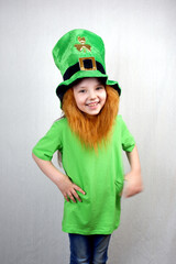 Pretty smiling littel girl in green clothes with decorative red beard in leprechaun's hat with gold clover leaf. Saint Patricks Day holiday motif