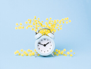 Minimal pastel spring poster. Alarm clock and mimosa flowers blue background.