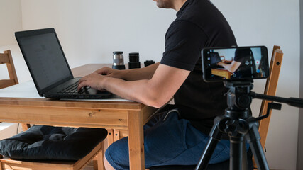 Young businessman sitting at a table at home working on a laptop and writing down ideas in a notebook