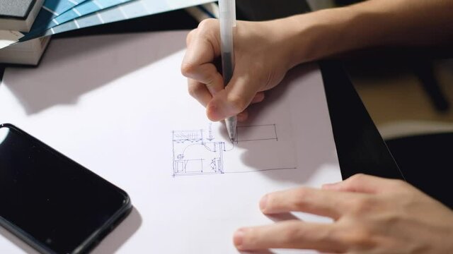 male architect drawing on blueprint using rulers and red pen on wooden working table.