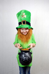 Smiling cute girl with red beard in green clothes, leprechaun's hat looking at cast iron leprechaun...