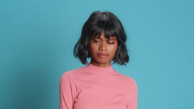 Sad beautiful young Asian woman with dark skin grimaces as if looking at something disgusting or ugly frown face with aversion dislikes something unpleasant poses against blue background.
