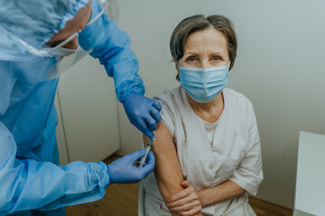 Doctor in protective overall and gloves making COVID-19 vaccination