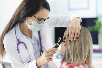 Otorhinolaryngologist examining patients sore ear with otoscope in clinic