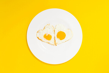 heart shaped fried eggs in a white plate on the yellow background.