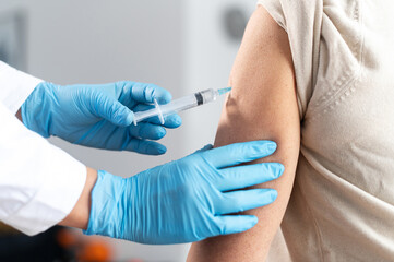 Close-up hands of the doctor wearing protective gloves giving a dose of new vaccine to senior patient indoors. A doctor, nurse injecting coronavirus remedy into an elderly people arm