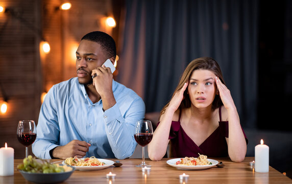Woman looking unhappy on date while boyfriend talking on cellphone in restaurant