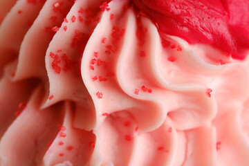 Close up macro texture of pink cupcake icing with red sprinkles for valentines day dessert concept.
